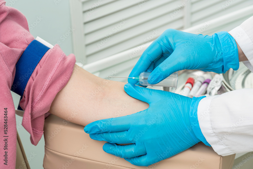 Obraz premium Cropped hands of nurse in blue gloves perform procedure for taking blood samples for analysis from patient's left arm.