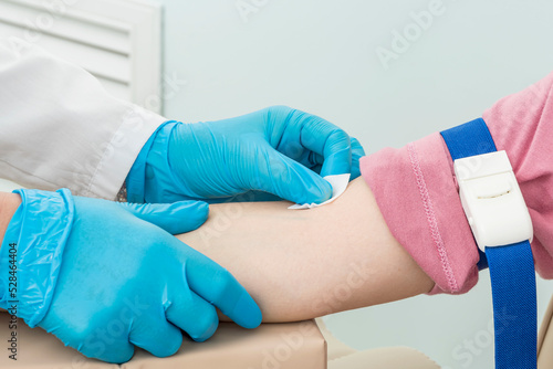Cropped hands of nurse in blue gloves wipe patient's right hand with alcohol wipe and prepare for blood sampling procedure.