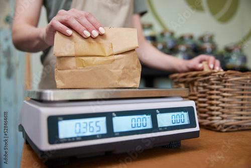 Close Up Of Sales Assistant In Sustainable Plastic Free Grocery Store Weighing Goods In Paper Bag On Digital Scales photo