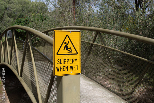 Slippery when wet yellow warning sign on the metal bridge in the park