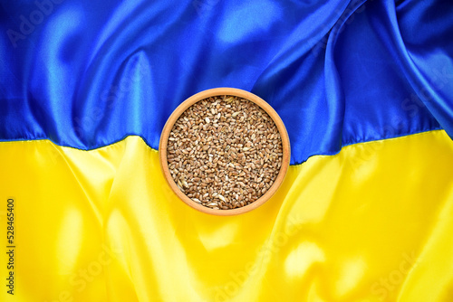 Bowl with wheat grains on the background of the flag of Ukraine. Concept of food supply crisis and global food scarcity because of war in Ukraine.
