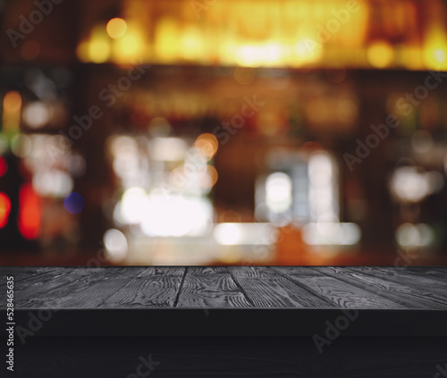 Empty black wooden surface and blurred view of bar interior. Space for design