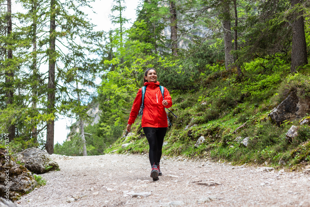 Free and happy alone. Cheerful woman hiking in the woods in red raincoat