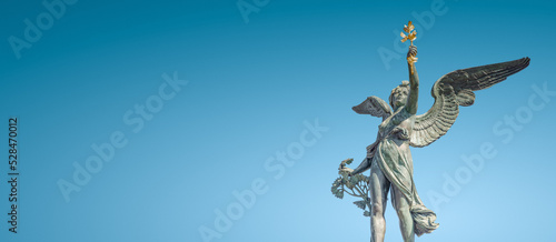 Banner with Statue of beautiful angel  at the top of column on the Cechuv Most Bridge in Prague, Czech Republic, at blue sky gradient background. Concept of religious and historical heritage.