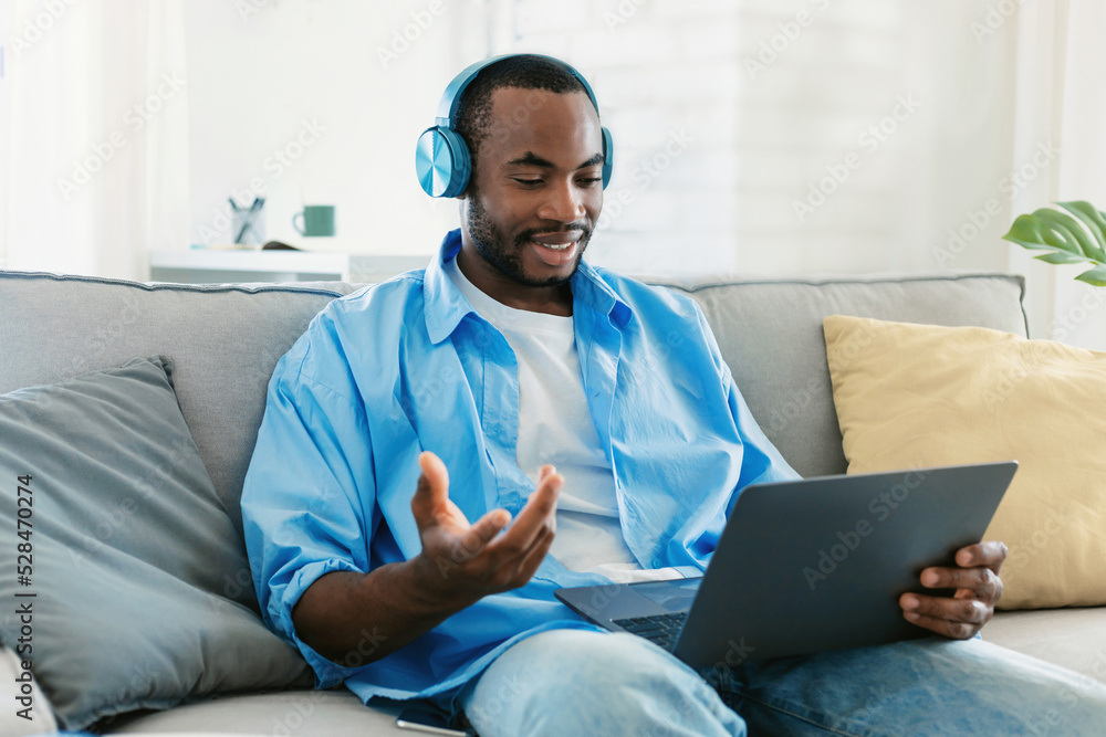 Freelancer african american man video calling via laptop, wearing headphones and talking to webcamera Freelancer african american man video calling via laptop, wearing headphones and talking to webcamera
