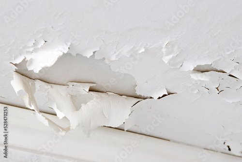 Swelling leaking of whitewash and plaster on ceiling of dwelling due to penetration of water from the top floor or roof, selective focus closeup.