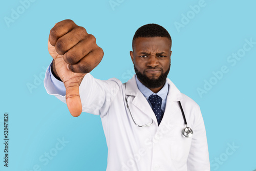 Displeased Black Male Doctor Showing Thumb Down Gesture At Camera © Prostock-studio