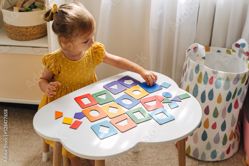 A little girl playing with wooden shape sorter toy on the table in playroom. Educational boards for Color and Shapes sorting for toddler. Learning through play. Developing Montessori activities. photo