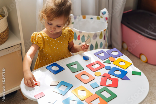 Billede på lærred A little girl playing with wooden shape sorter toy on the table in playroom