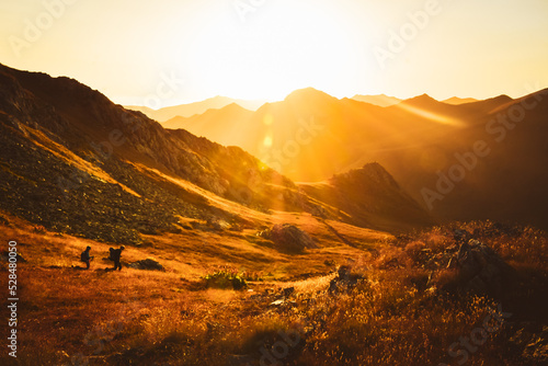 Man and woman hikers in distance hike on trail outdoors on beautiful sunset in autumn together against sun. Cinematic inspirational active people on trek in caucasus mountains