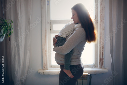 Pregnant mom holding and hugging crying toddler baby.