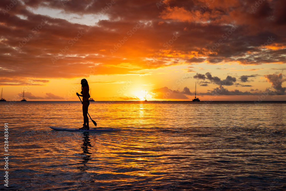Silhouette of a woman on a stand up paddle (SUP) board during a colorful sunset and calm sea