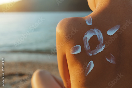 The sun drawing sunscreen ,suntan lotion on boy back. Little boy with sunscreen cream on the shoulder in sun shaped against of the sea. Concept of skincare and protection.