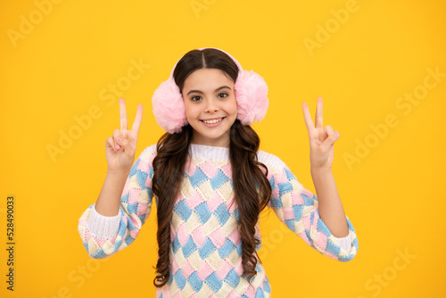 Teenager girl with winter warm earmuff ear-flaps hat over isolated yellow background. Winter christmas holidays, new year mood. Kids warm clothes.