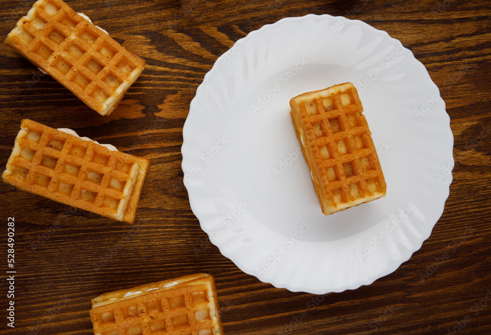 Viennese waffles lie on and next to a white plate. Viennese waffles lie on and next to a white plate.