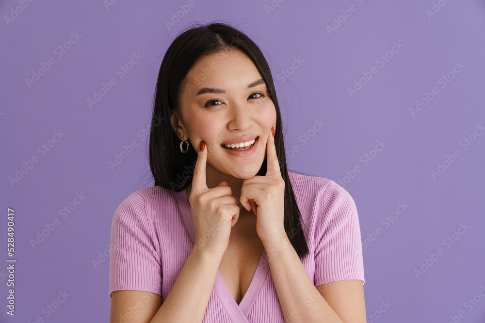 Asian young woman smiling and pointing fingers at her cheek Asian young woman smiling and pointing fingers at her cheek