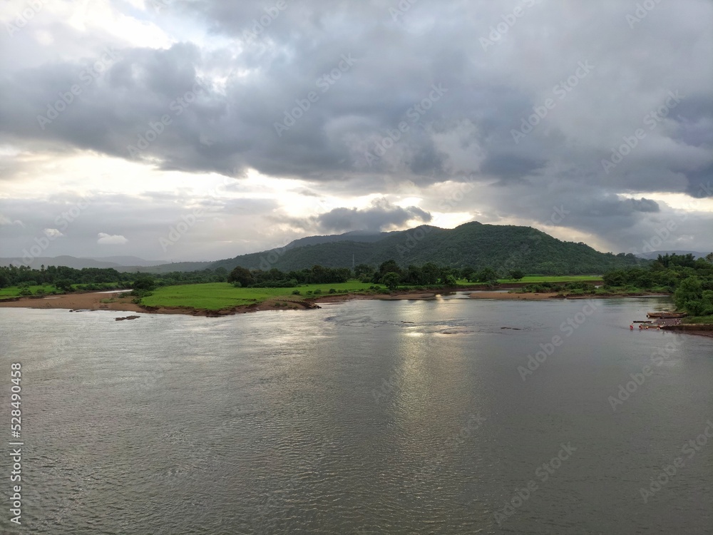 beautiful river near mountain under cloudy sky and a rice field