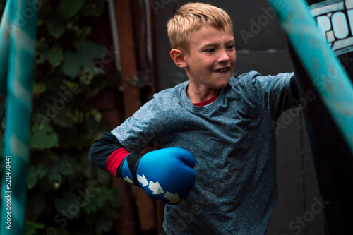 Vászonkép a boy punches a punching bag in blue gloves in the yard