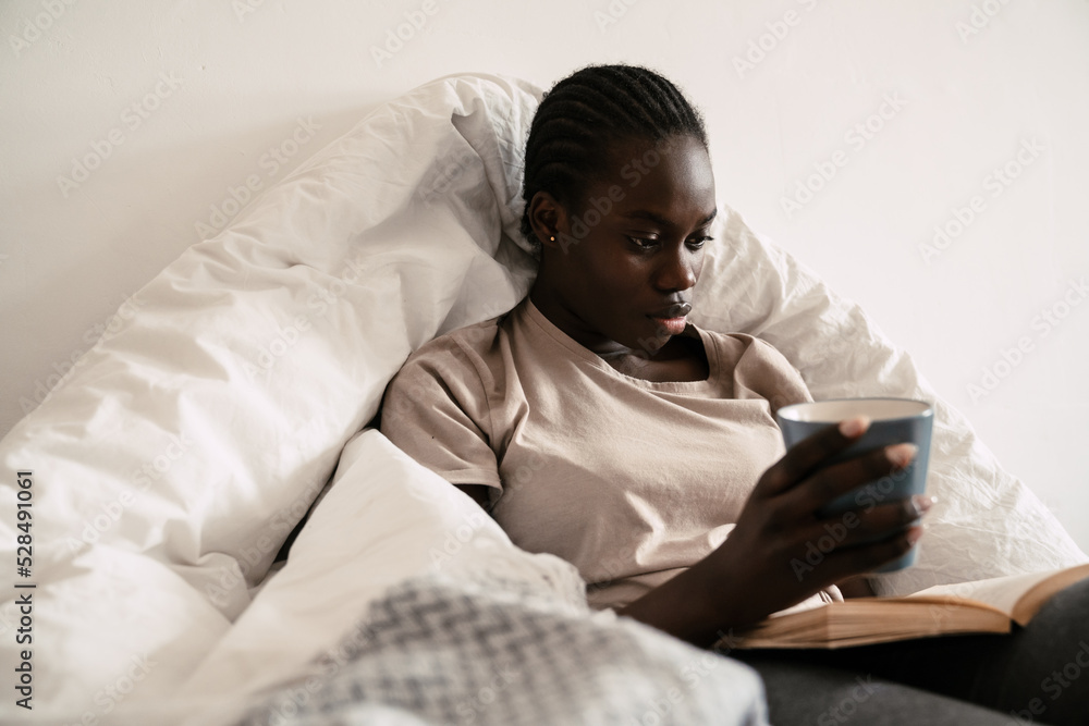 Young beautiful african woman reading a book and holding cup Young beautiful african woman reading a book and holding cup