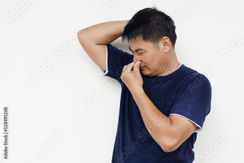 Closeup Asian man covers his nose for his bad odor armpit, isolated on white background.  Concept : health problem. Unpleasant body odor , smell nasty reaction.  Negative emotion.                      photo