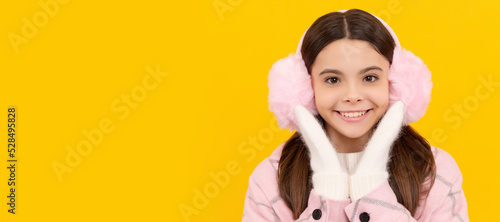 Winter girl. happy kid in winter mittens and earmuffs on yellow background, winter. Banner of christmas child girl, studio kid winter portrait with copy space.