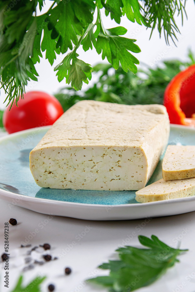 Sliced tofu soy cheese on a cutting board with basil, spices and vegetables
