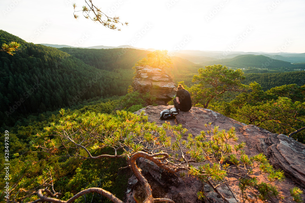 Mädchen sitzt zum Sonnenuntergang auf einem Felsen im Pfälzerwald in Rheinland Pfalz in Deutschland