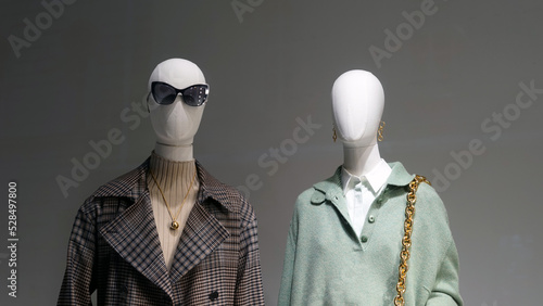 Mannequins installed in the window of a fashion store demonstrate samples of seasonal clothing.
