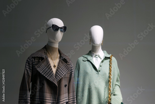 Mannequins installed in the window of a fashion store demonstrate samples of seasonal clothing.