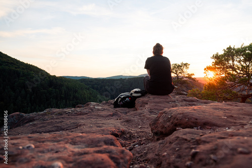 Mädchen sitzt zum Sonnenuntergang auf einem Felsen im Pfälzerwald in Rheinland Pfalz in Deutschland