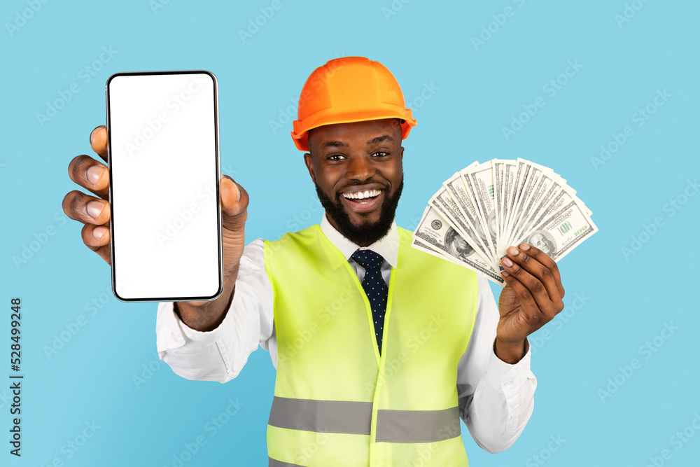 Black Man In Hard Hat And Vest Holding Money And Blank Smartphone Black Man In Hard Hat And Vest Holding Money And Blank Smartphone