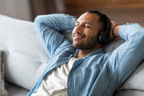 Handsome Smiling Black Man Listening Music In Wireless Headphones At Home