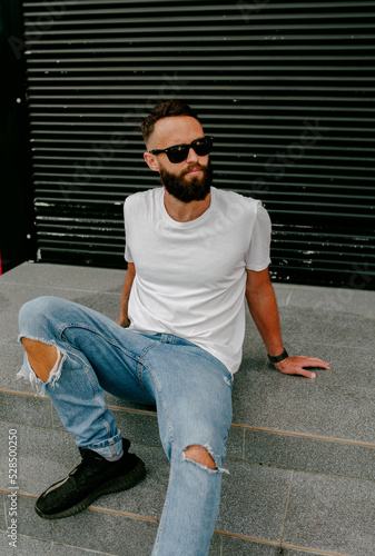 Young bearded hipster guy wearing white blank t-shirt and blue jeans in a random urban style. Design men t shirt mock-up for print