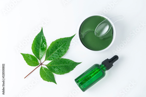 A green face serum or essential oil made of grapes and eye antiaging patches lying on a white background