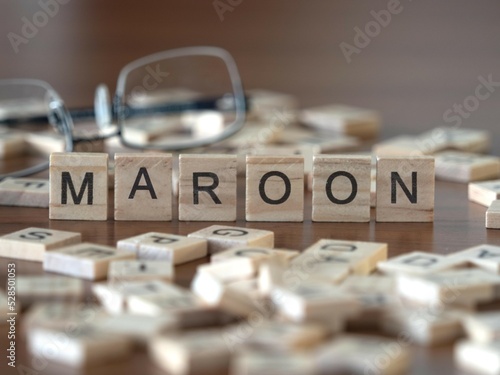 maroon word or concept represented by wooden letter tiles on a wooden table with glasses and a book