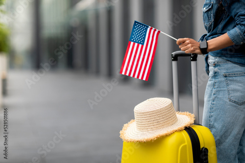 Woman with straw hat on luggage holding flag of US