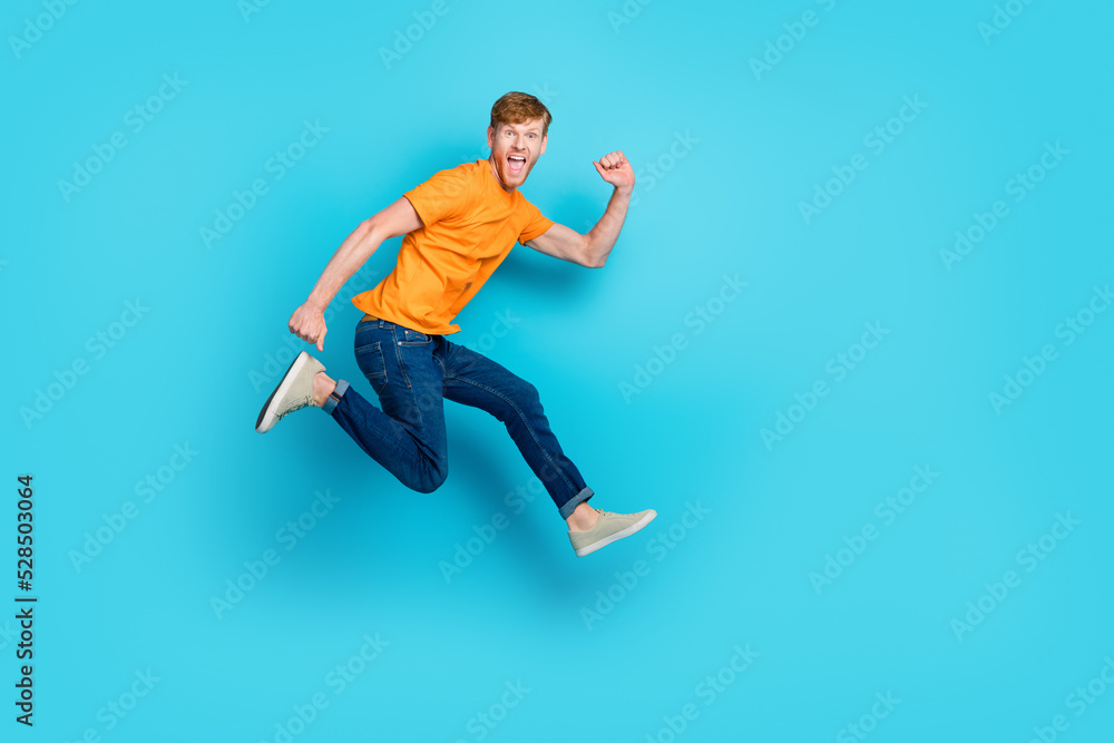 Full length profile photo of impressed red hair guy jump wear t-shirt jeans boots isolated on blue color background