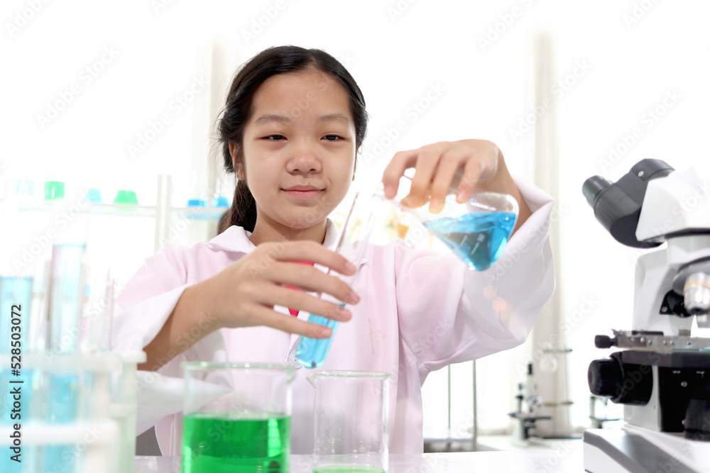 Adorable Asian schoolgirl in lab coat do science experiments, pouring blue reagent solution from beaker into test tube, happy young scientist kid have fun during doing experiments, kid education Adorable Asian schoolgirl in lab coat do science experiments, pouring blue reagent solution from beaker into test tube, happy young scientist kid have fun during doing experiments, kid education