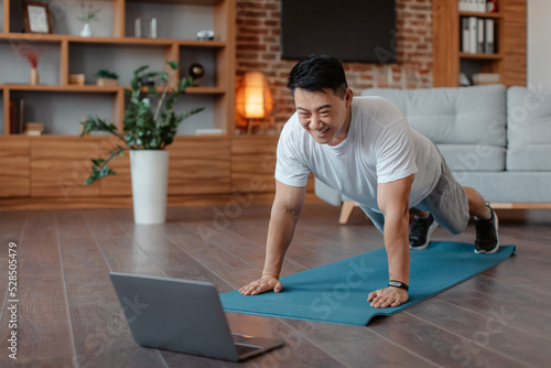 Home workout concept. Mature asian man exercising with laptop computer online standing in plank, free space