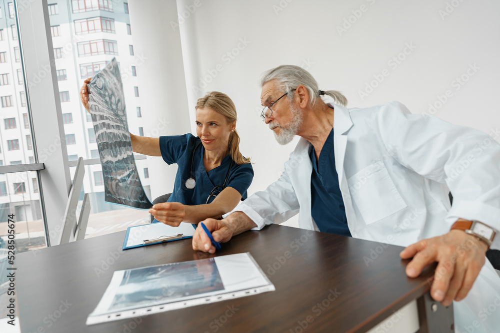 Obraz premium Team of doctors looking on results of X-Ray or MRI scan of patient's spine in medicine office