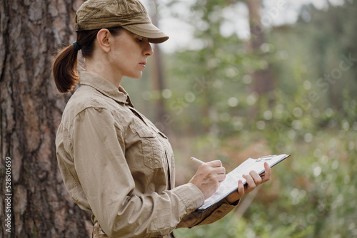 Canvas Print A woman forester in uniform with a clipboard monitoring national park area in summer, selective focus