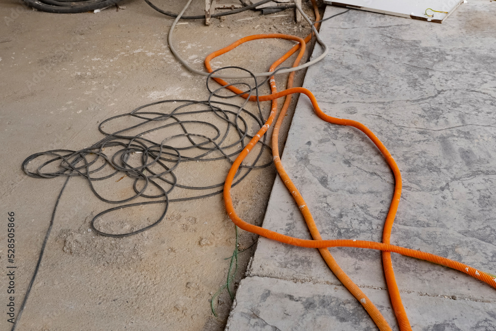 orange and black electric cables lie on the concrete floor of an