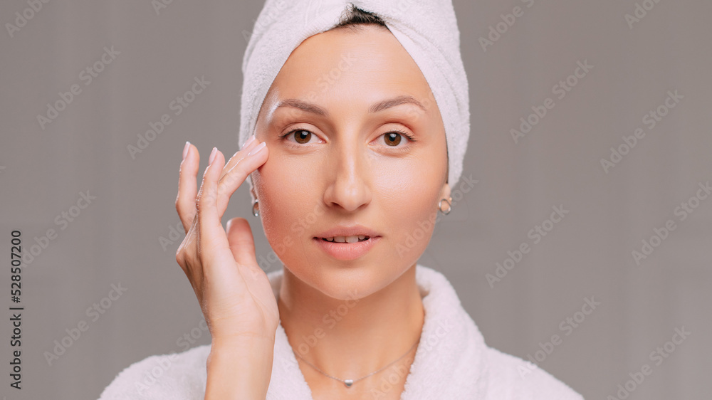 Young attractive woman in a bathrobe applies cream on her face in the bathroom. Close-up of the face. Young attractive woman in a bathrobe applies cream on her face in the bathroom. Close-up of the face.