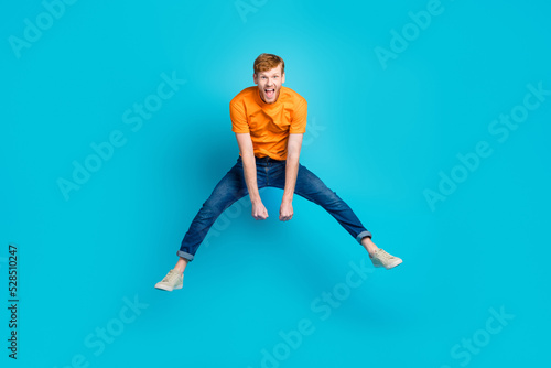 Full body photo of impressed ginger hair guy jump wear t-shirt jeans sneakers isolated on blue color background