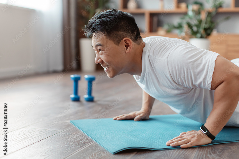 Athletic korean mature man doing push-ups on sports mat at home, working out core and hands muscles, copy space Athletic korean mature man doing push-ups on sports mat at home, working out core and hands muscles, copy space