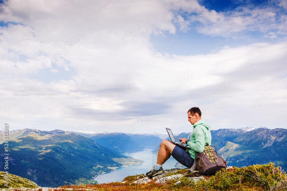 Young man sitting on the cliff using laptop Young man sitting on the cliff using laptop
