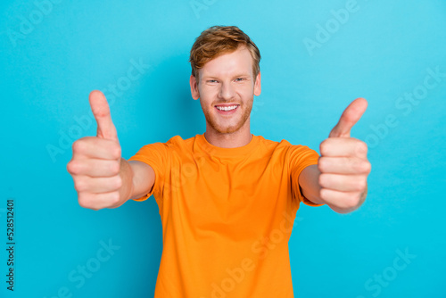 Photo of positive cheerful guy with ginger hairstyle wear orange t-shirt thumbs up at camera to you isolated on turquoise color background © deagreez