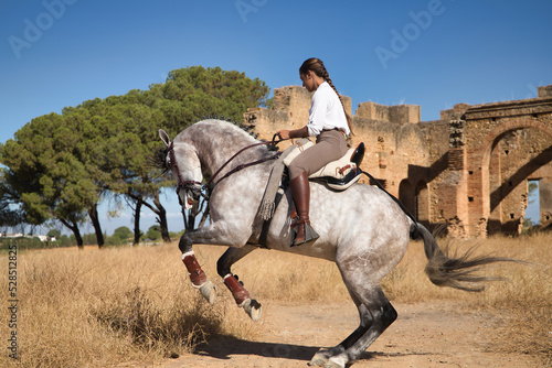 Young beautiful woman performing turns riding her horse in the countryside next to an abandoned and ruined building on a sunny day. Concept horse riding, animals, dressage, horsewoman.