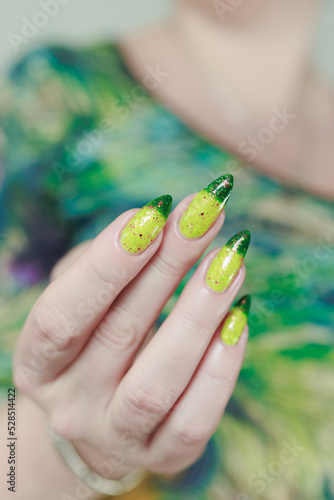 Woman's hand with long nails and bright yellow green thermo manicure with bottles of nail polish photo