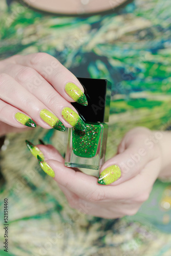 Woman's hand with long nails and bright yellow green thermo manicure with bottles of nail polish photo